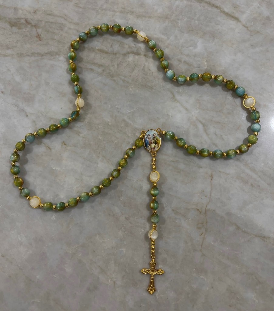 Green and gold cat-eye rosary with cream accent beads, a Holy Family center, and an ornate gold cross.