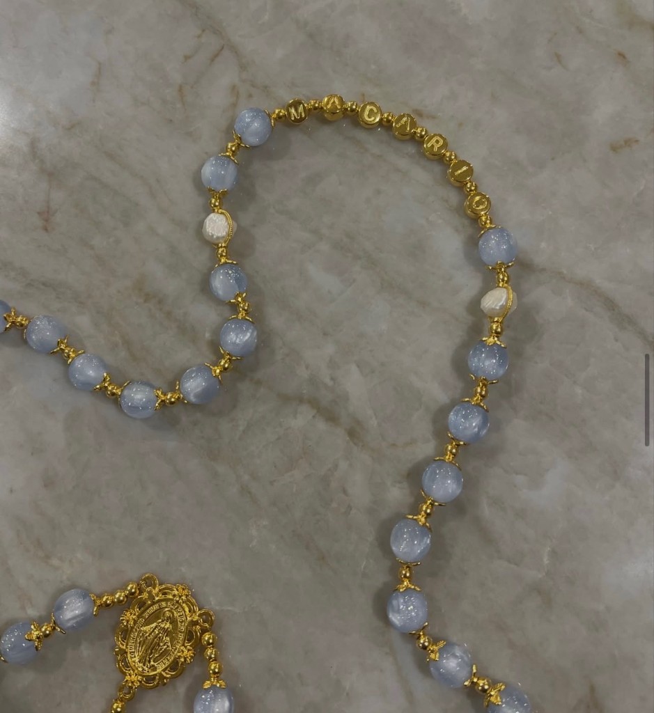Gold letter beads spelling MACARIO on a light blue rosary.