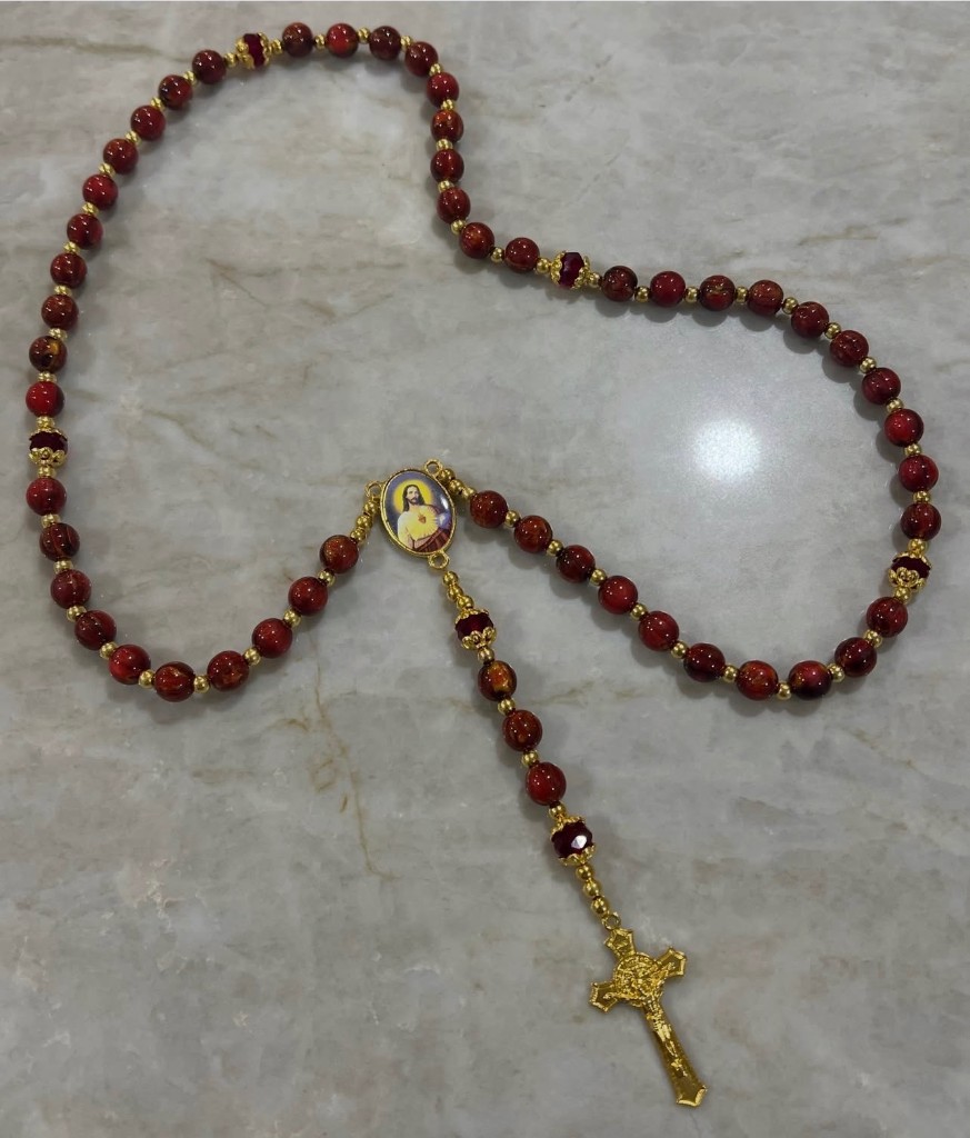 Deep red bead rosary with faceted accent beads, a Sacred Heart of Jesus center, and a gold crucifix.