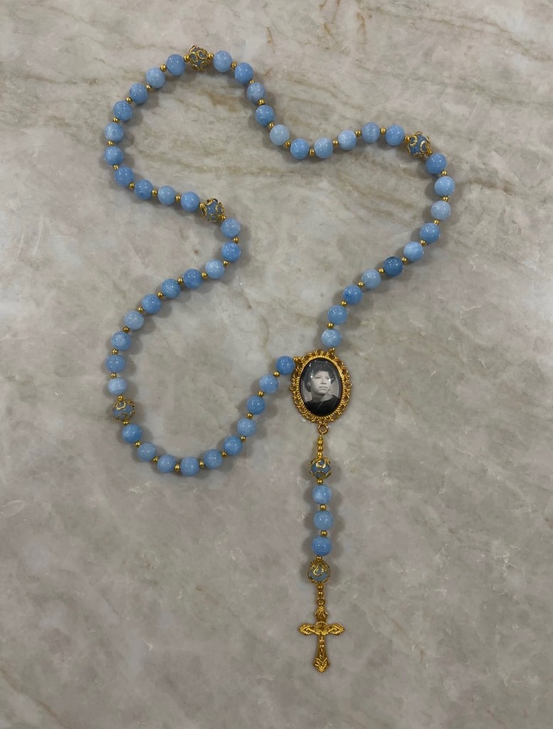 Light blue bead rosary with gold filigree accent beads, a custom photo center, and an ornate gold cross.